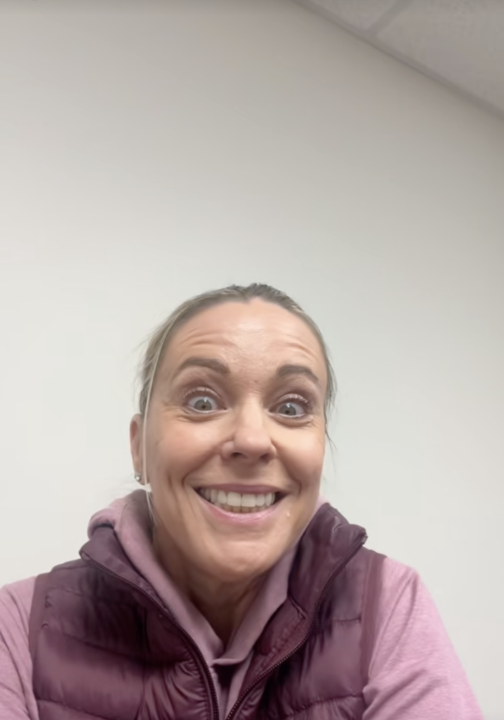 Kate Gosselin making a wide-eyed, smiling face, wearing a purple hooded sweatshirt and a darker purple vest.