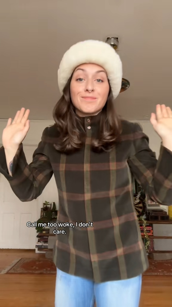 A woman in a white hat and plaid jacket raises her hands.