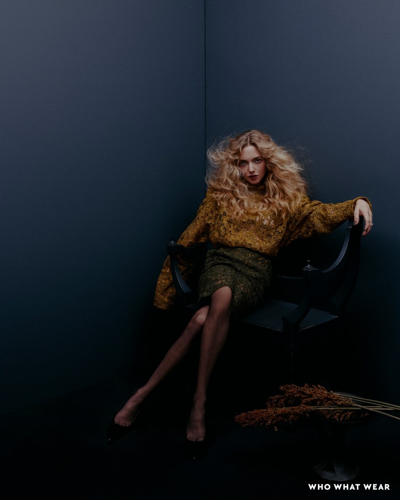 Amanda Seyfried sitting on a chair, wearing a golden blouse and green skirt.