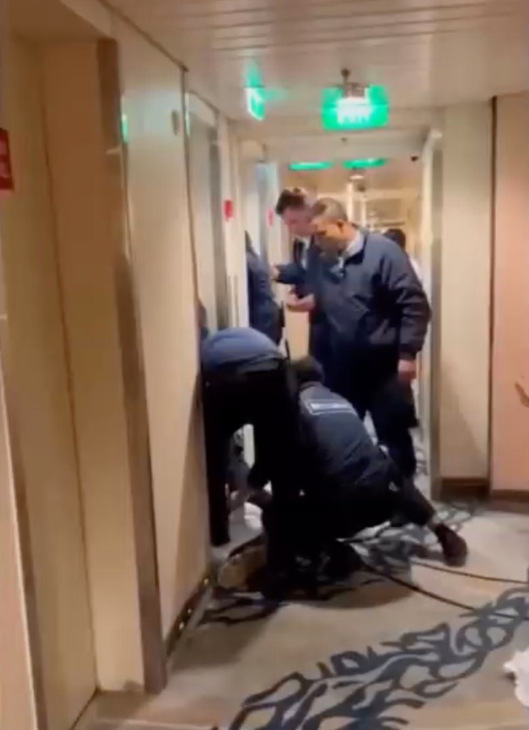 Cruise ship crew members restraining a man on the floor of a hallway.