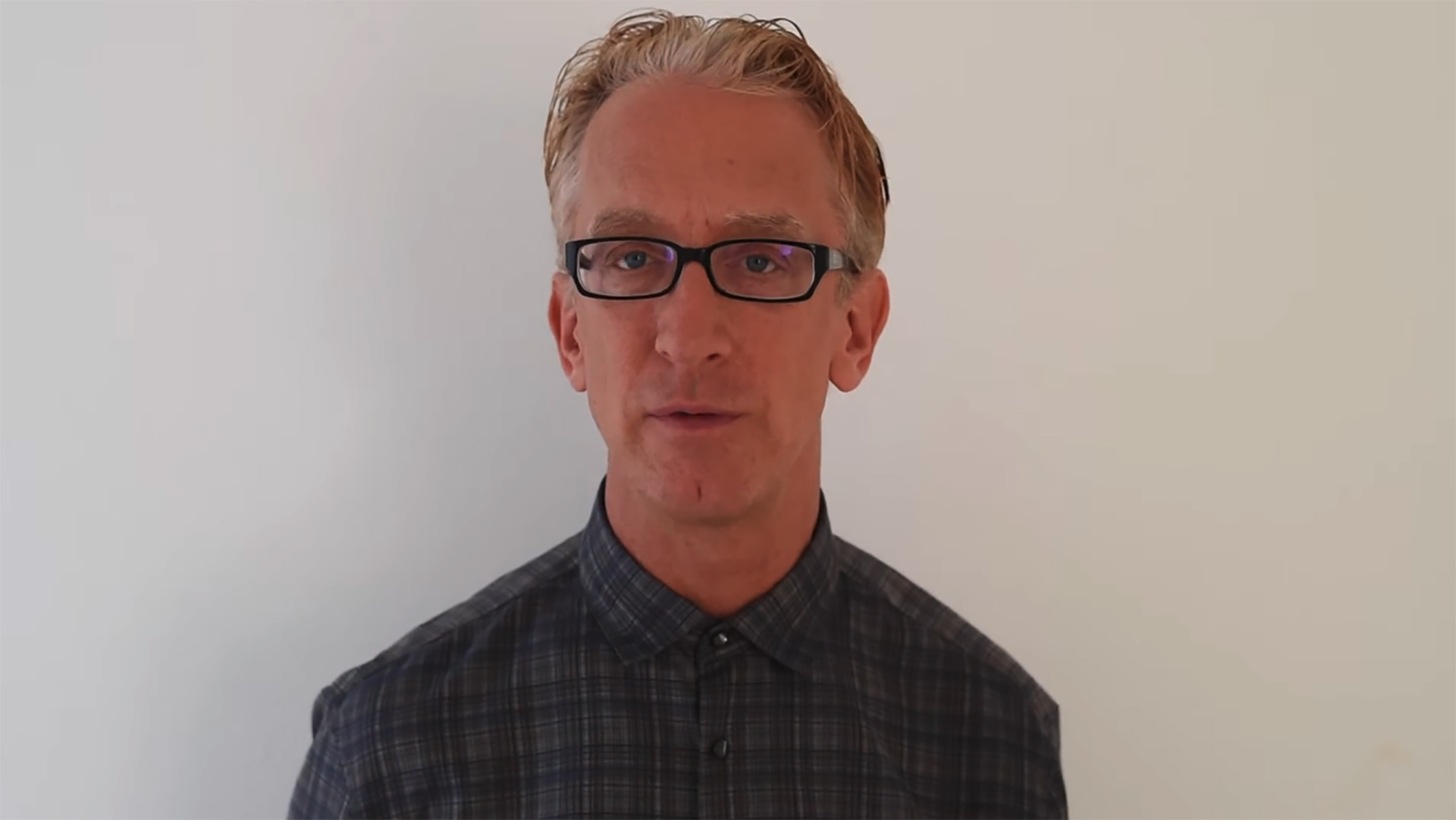 Andy Dick wearing glasses and a plaid shirt.