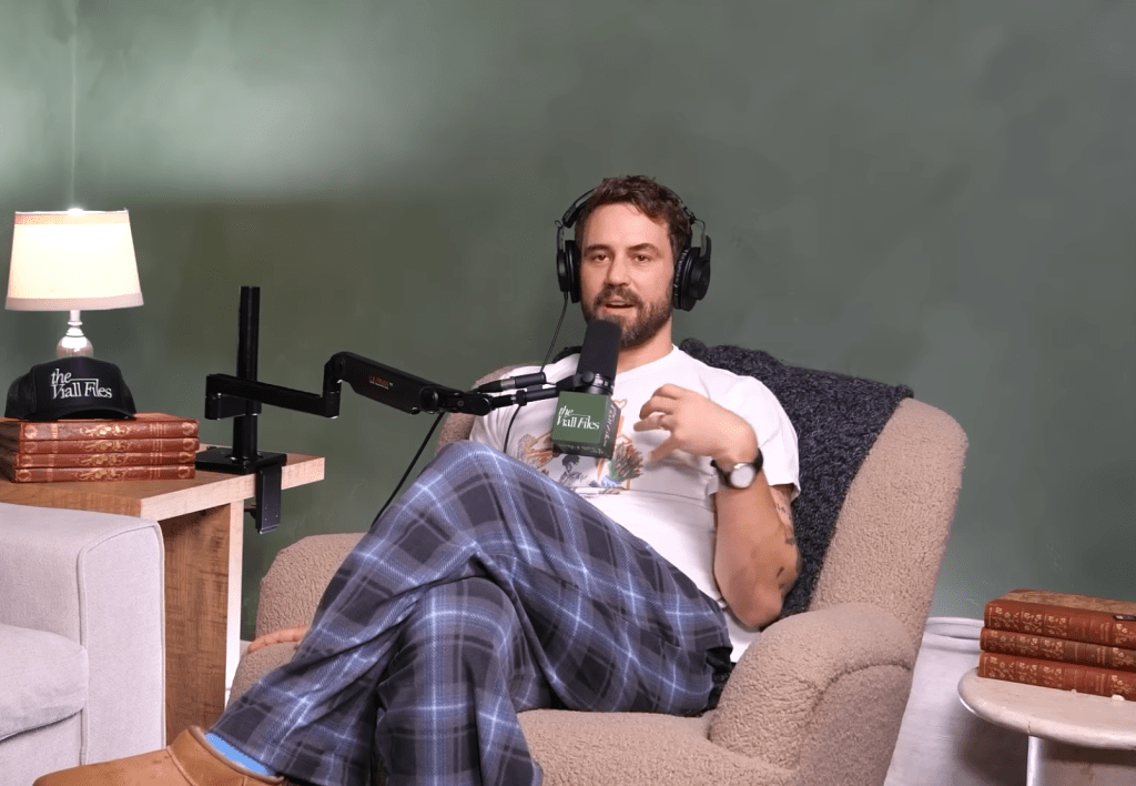 Nick Viall wearing headphones and holding a microphone while sitting in a chair.
