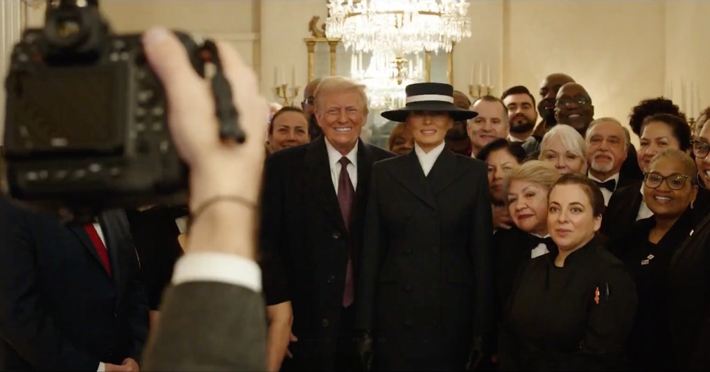 Donald and Melania Trump posing for a photo with a group of people, with a camera in the foreground.