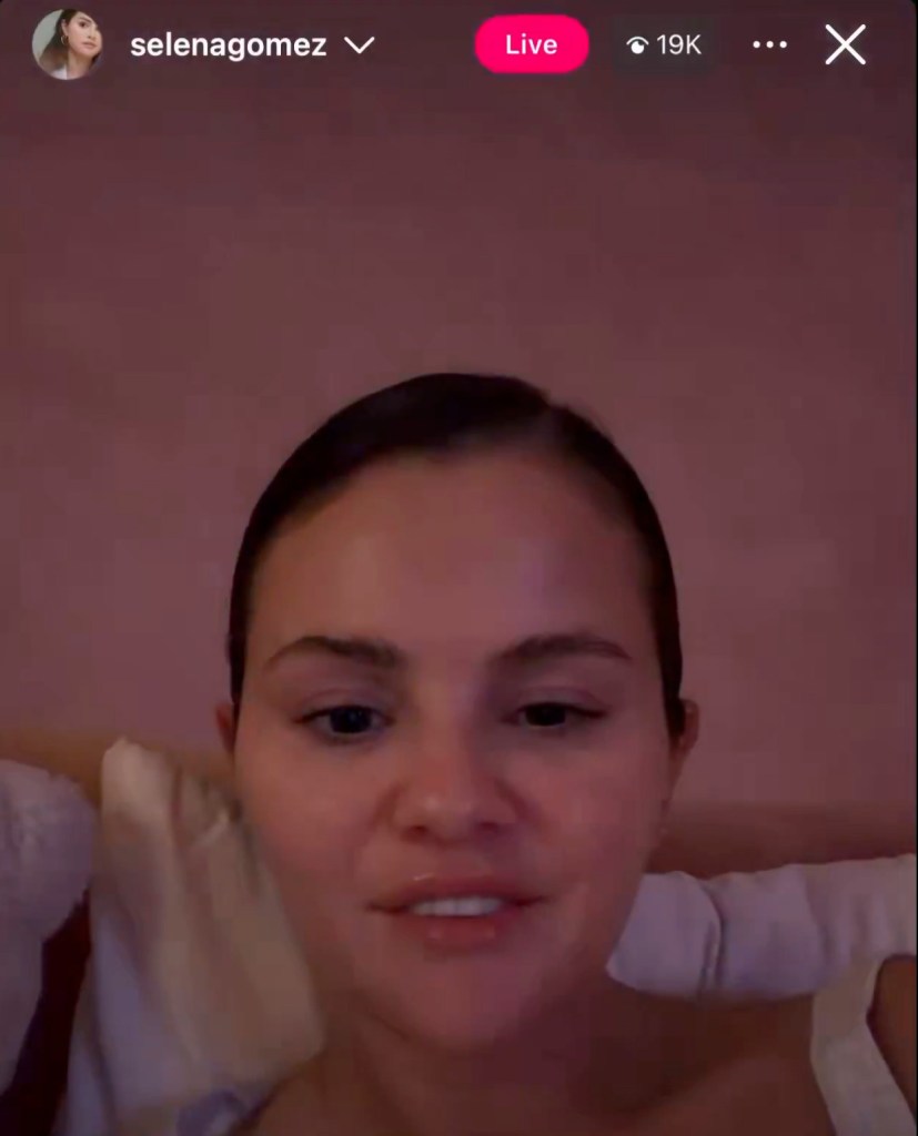 Selena Gomez in an Instagram Live video, wearing white pajamas, with pink lighting.