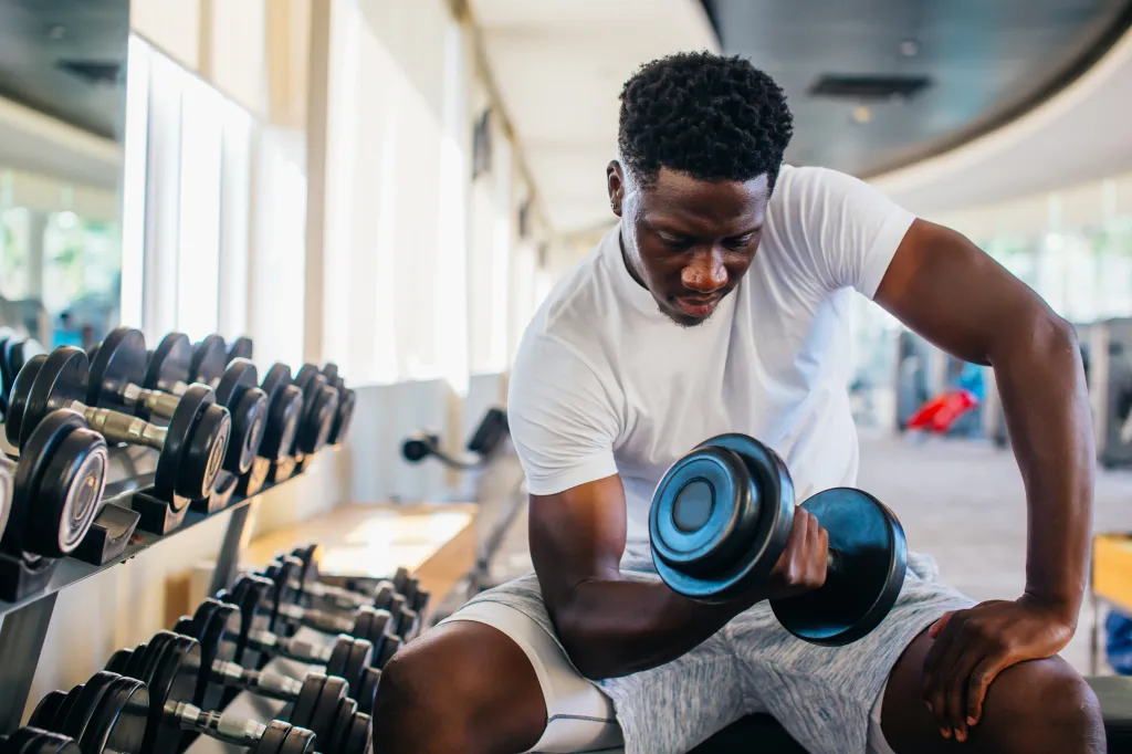 Young African American man sitting and lifting a dumbbell in a gym.