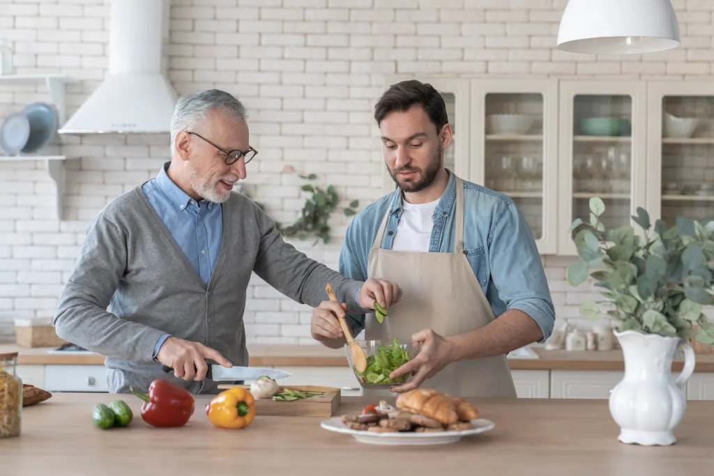 Son and senior father cooking together in a kitchen.
