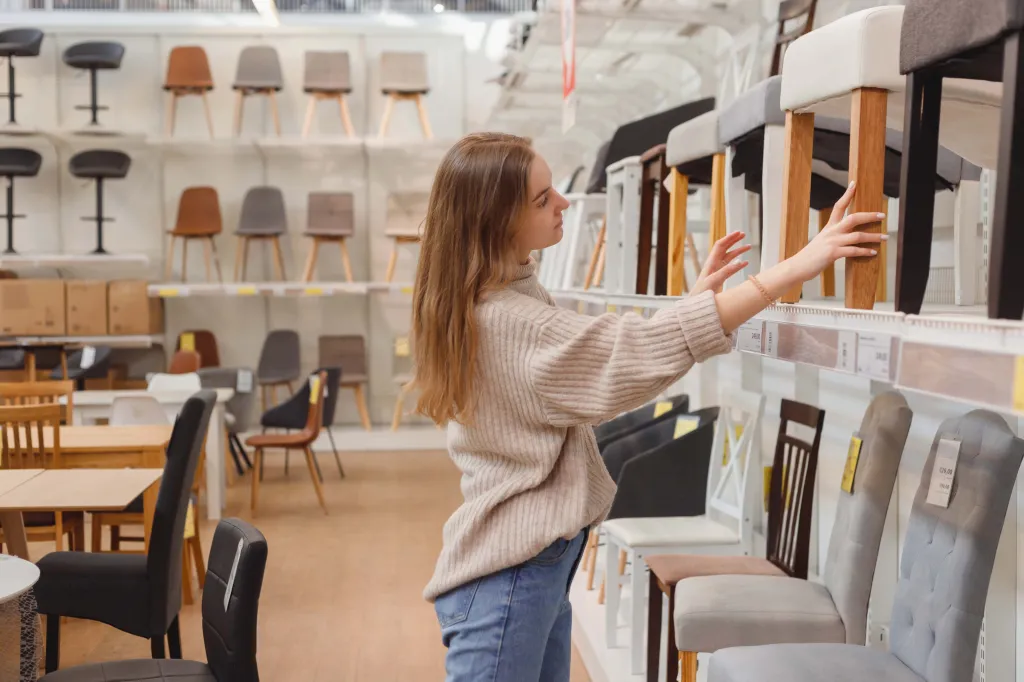 A young woman comparing chairs on display in a furniture store.