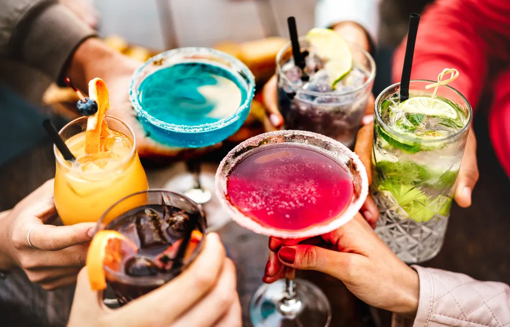 People toasting multicolored fancy drinks.