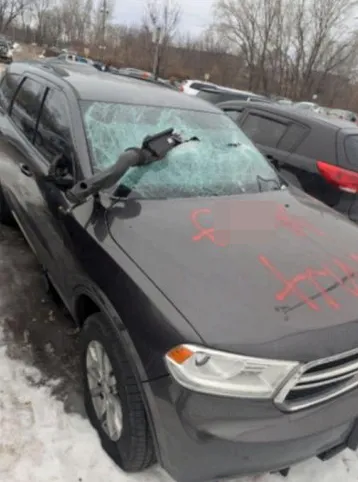 Vandalized vehicle with a shattered windshield and graffiti on the hood.