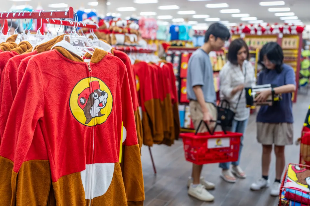 Red and brown Buc-ee's apparel on display in a store, with customers shopping in the background.