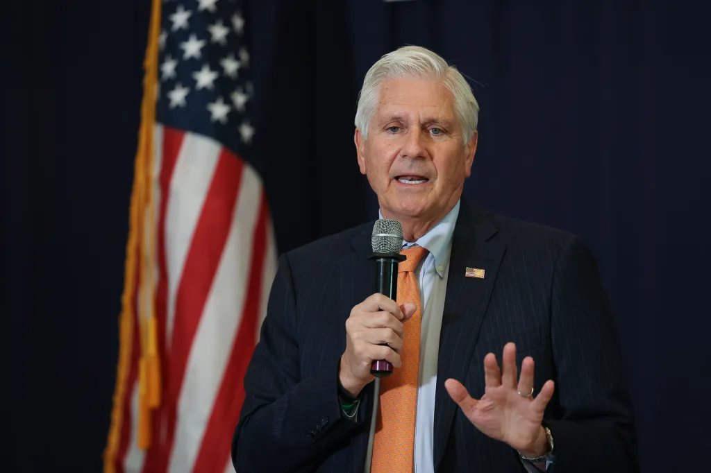 Nassau County Executive Bruce Blakeman speaking with a microphone in front of an American flag.