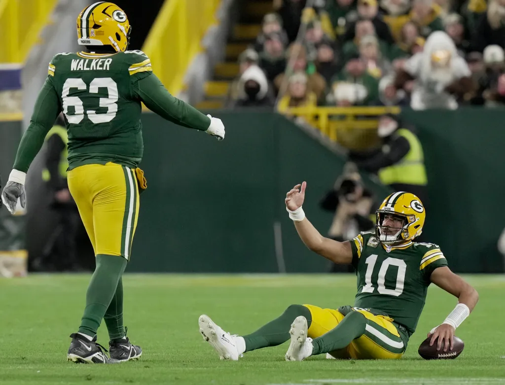 Green Bay Packers quarterback Jordan Love (10) sits on the turf after being sacked, as offensive tackle Rasheed Walker (63) stands nearby.