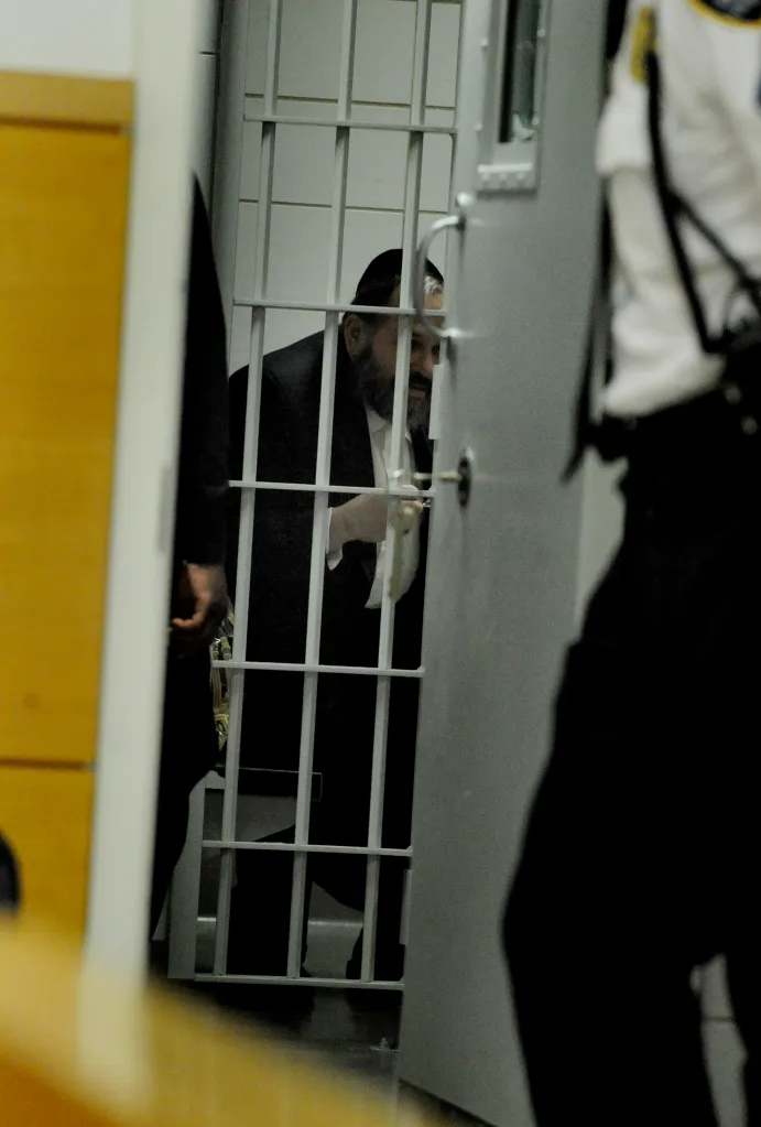 A rabbi with a dark beard and yarmulke seen through prison bars.