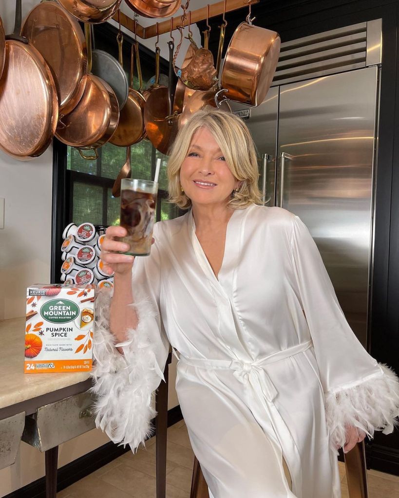 Martha Stewart holding a glass of iced coffee while wearing a white feathered robe, next to a box of Green Mountain Pumpkin Spice K-Cups.