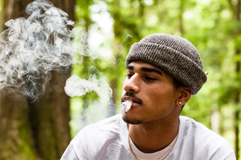 A young man in a beanie smoking a blunt outdoors.