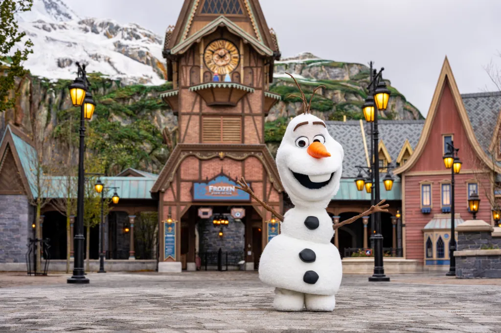 Olaf the snowman character from Frozen standing in a themed village.