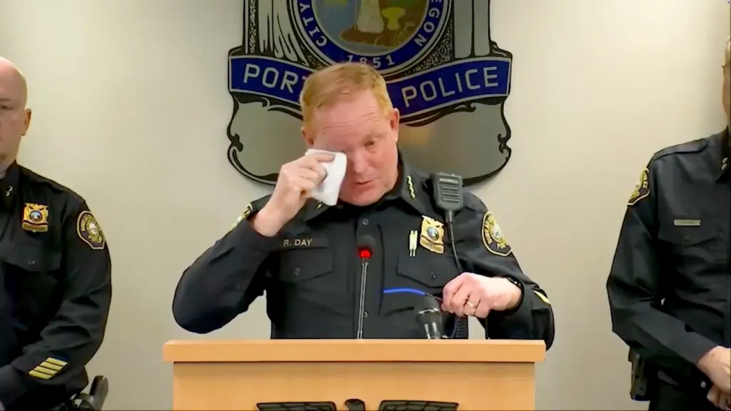 A police officer at a podium wipes away a tear with a tissue.