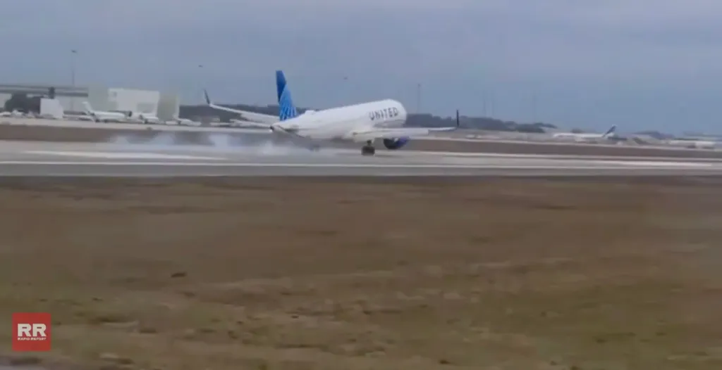 A United airplane lands on a wet runway, kicking up spray.