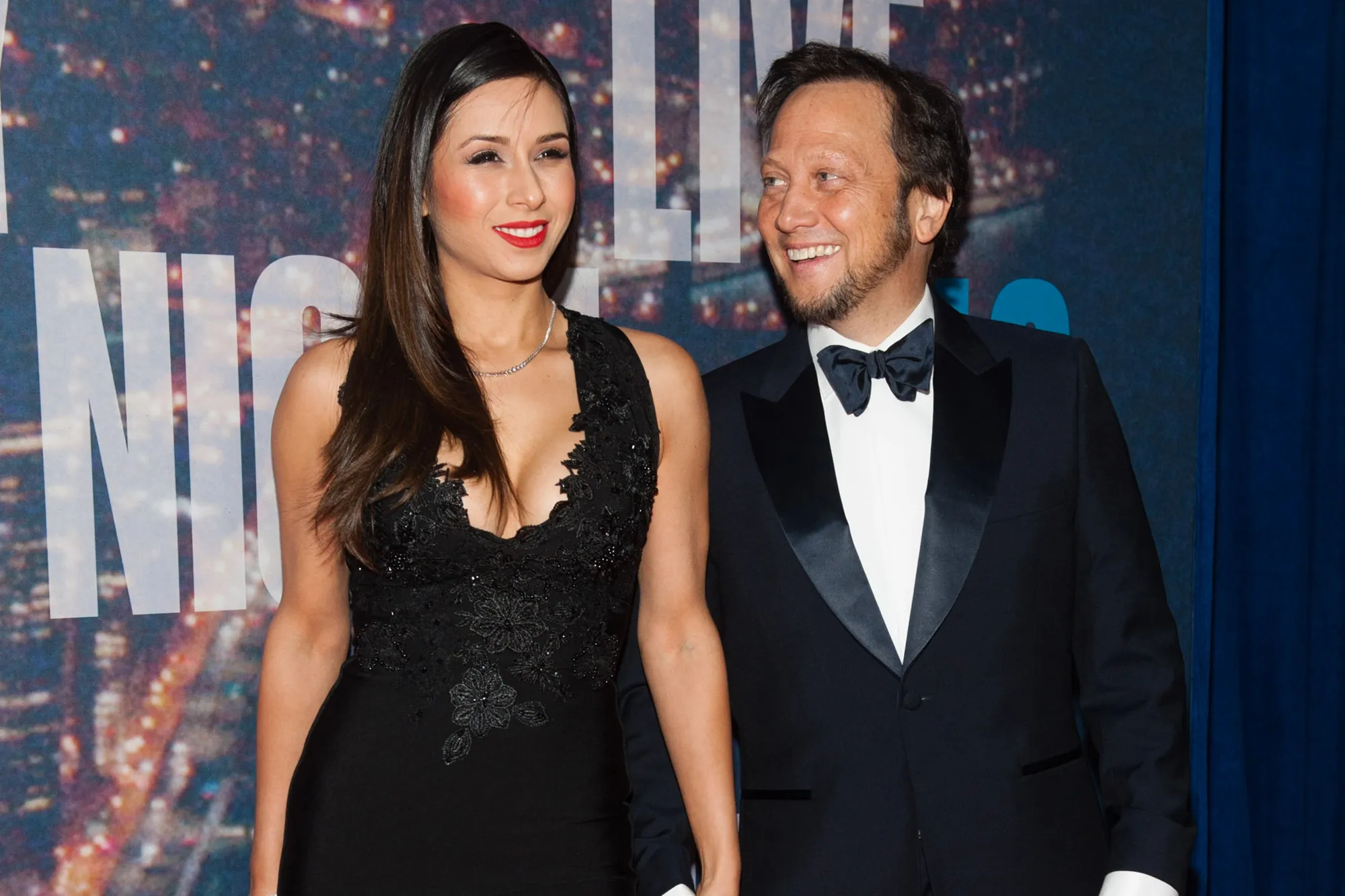 Rob Schneider and his wife Patricia Azarcoya Arce smiling on a red carpet.