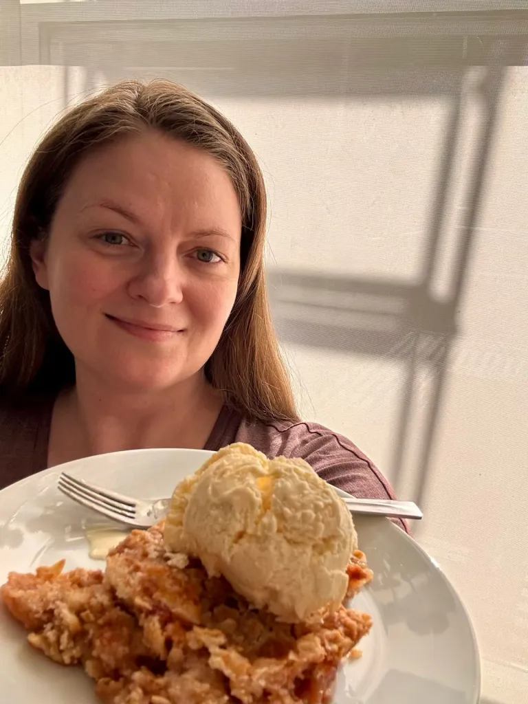 Celeste Komm holding a plate of apple crumble with a scoop of vanilla ice cream she made