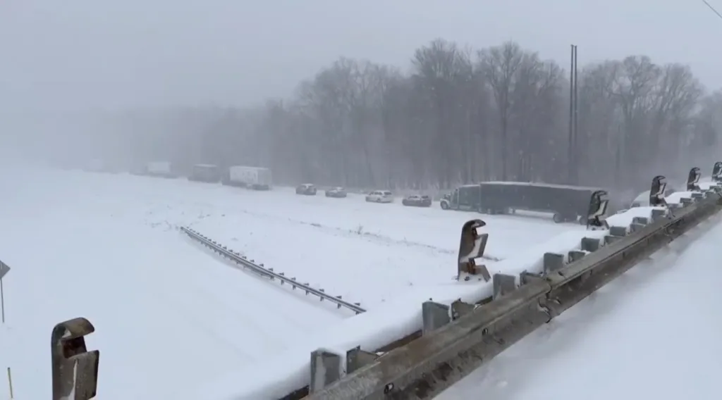 Snow-covered highway with vehicles stopped due to a multi-vehicle crash, with trees in the background.