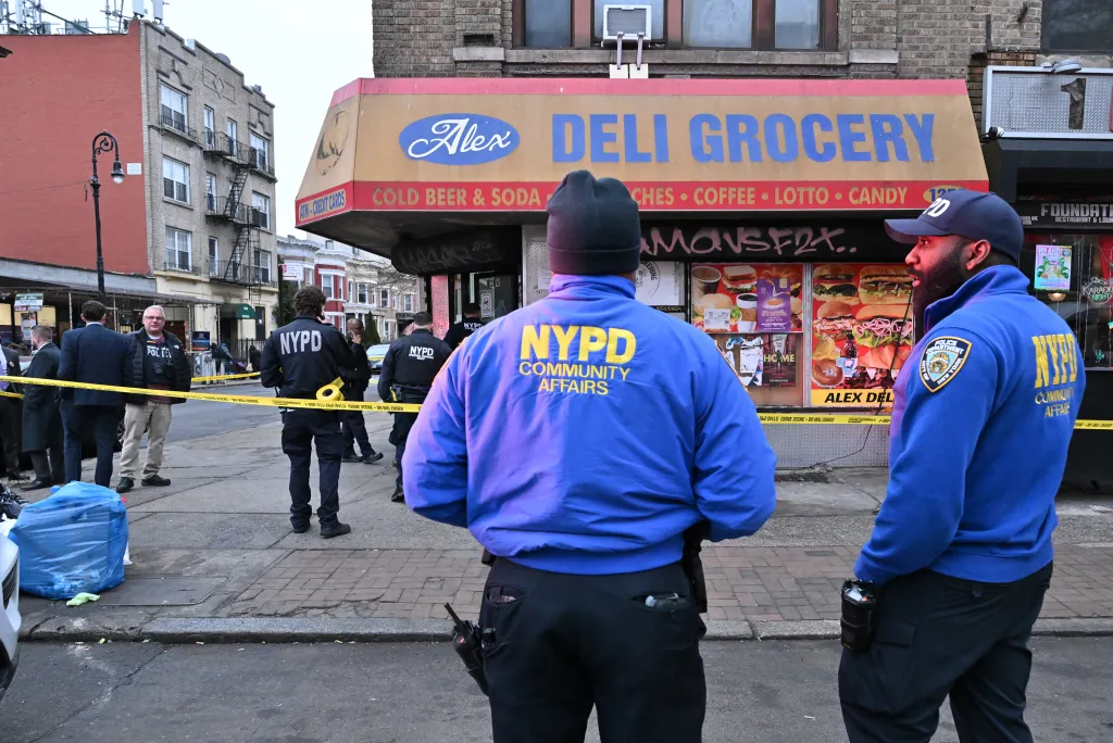 Two NYPD Community Affairs officers stand in front of Alex Deli Grocery, where a shooting occurred.