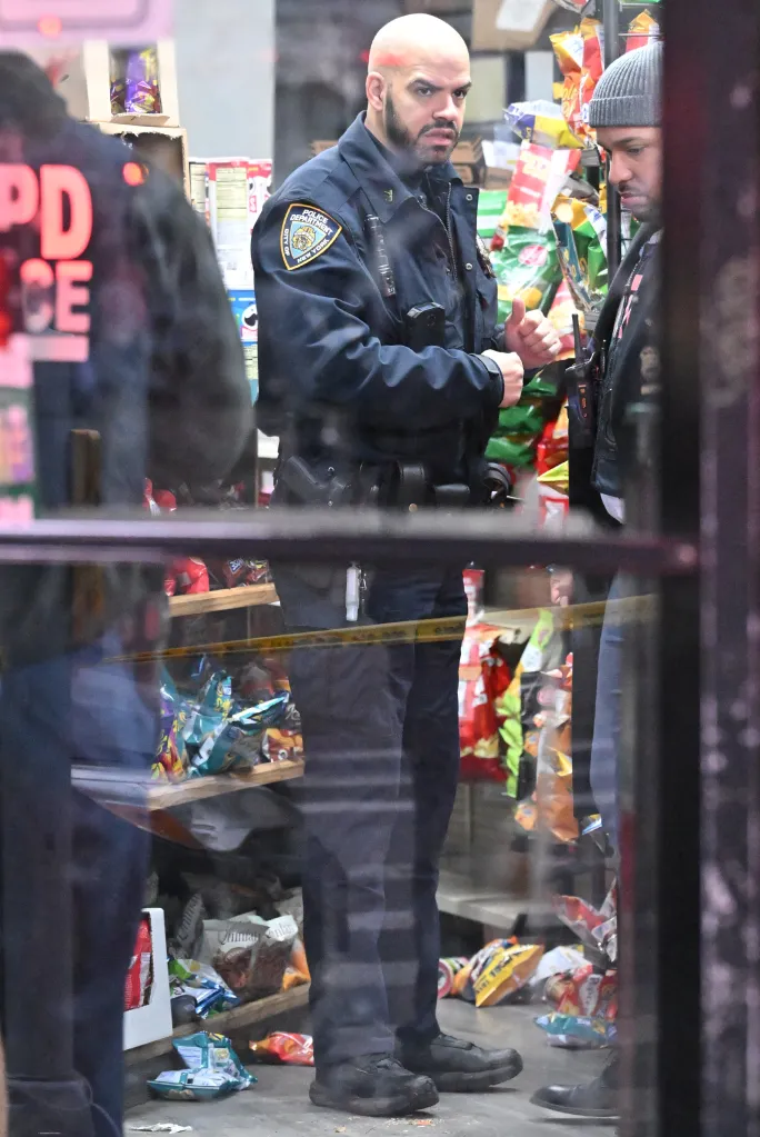 Police officers stand inside a deli where a shooting occurred, with snack bags on the floor and shelves.