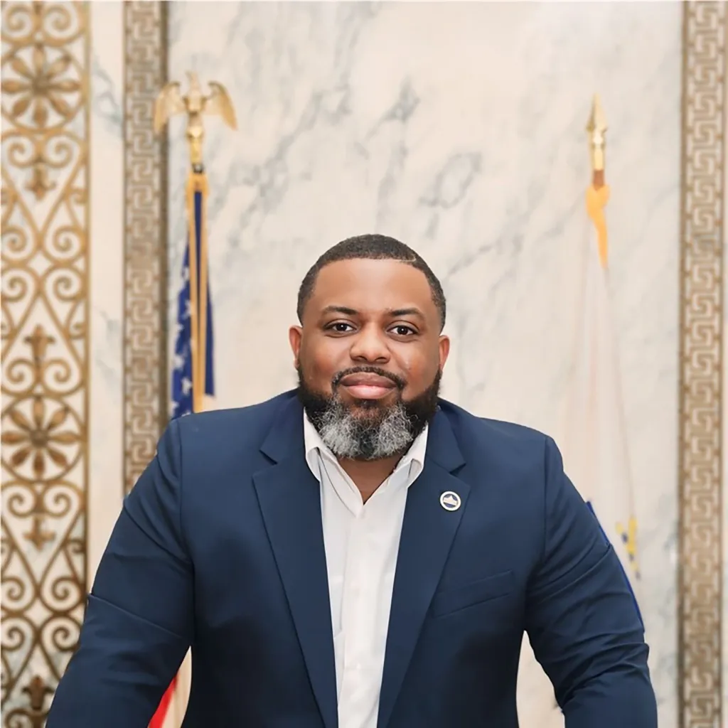 Man in a navy suit and white shirt with a salt and pepper beard and goatee.