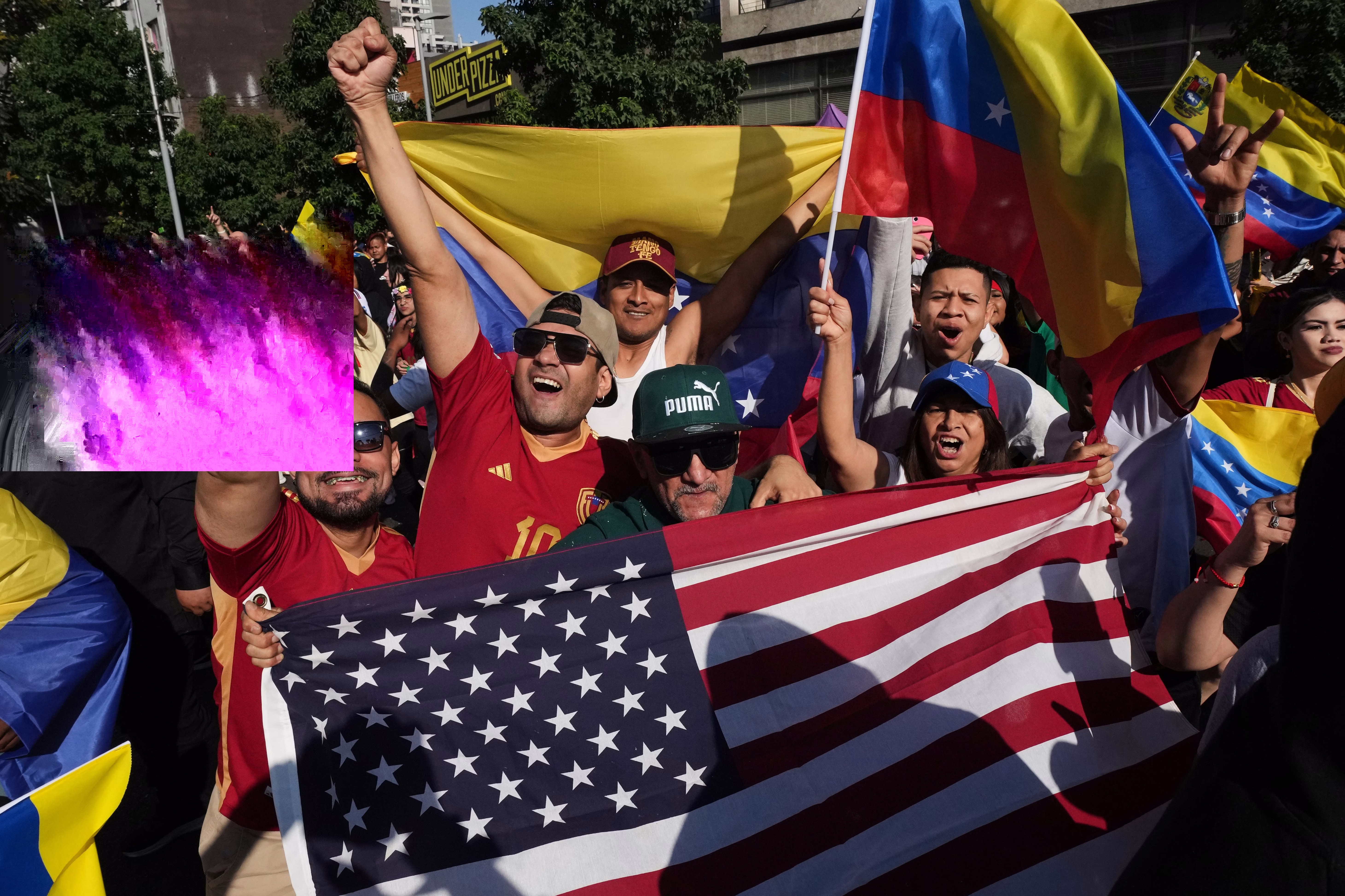 A crowd of people hold Venezuelan flags and an American flag in a public Square.
