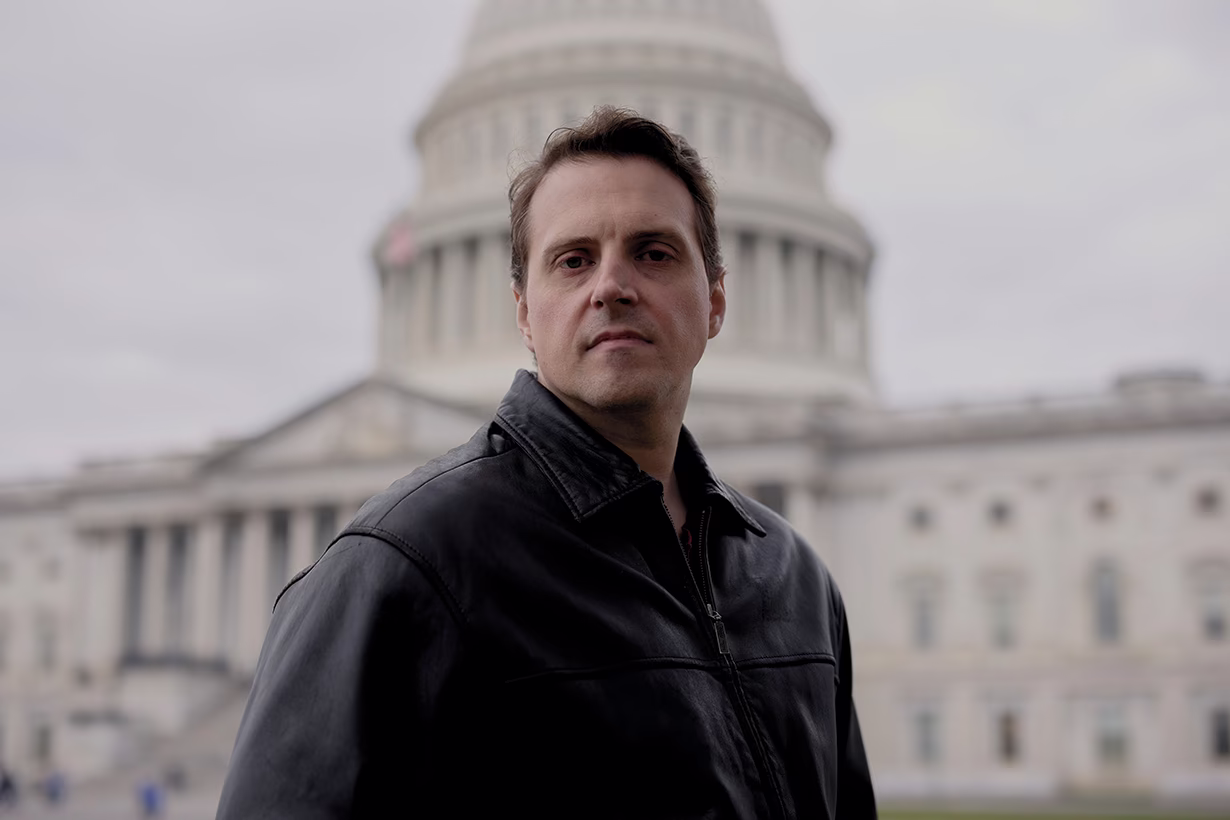 photo of same officer today, wearing black leather jacket and standing with Capitol building in background