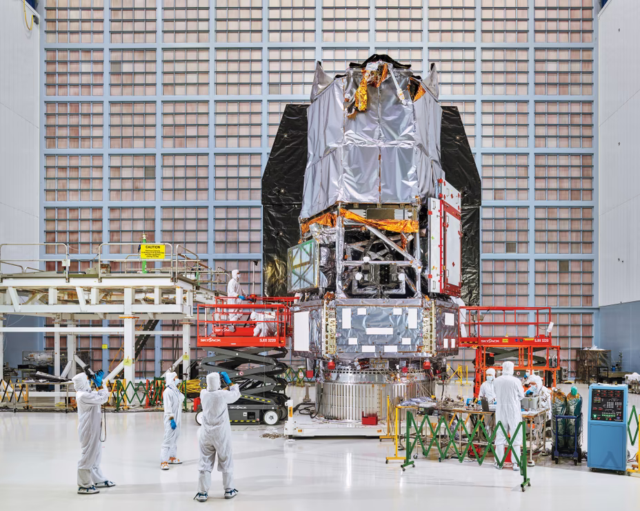 photo of enormous clean room with multi-story telescope under construction and clean-suit-clad scientists and engineers working on scissor lifts and taking photos around its base