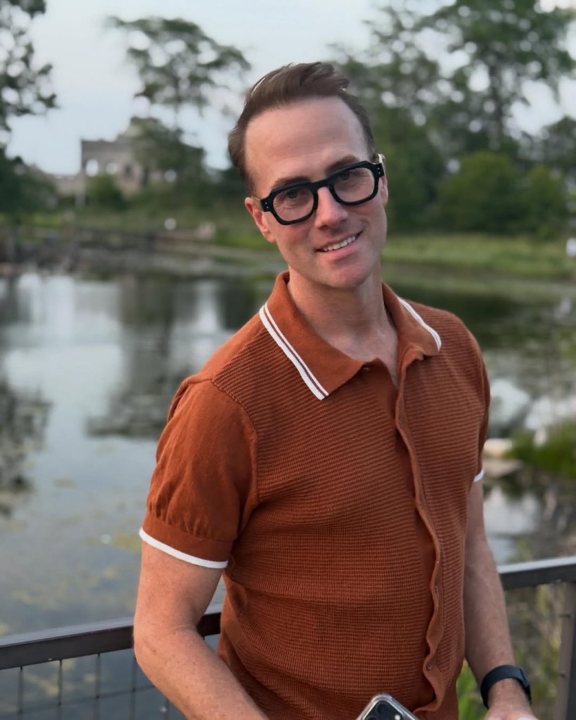 Bret Hanna-Shuford, a Broadway actor, smiling while wearing glasses and a brown shirt.