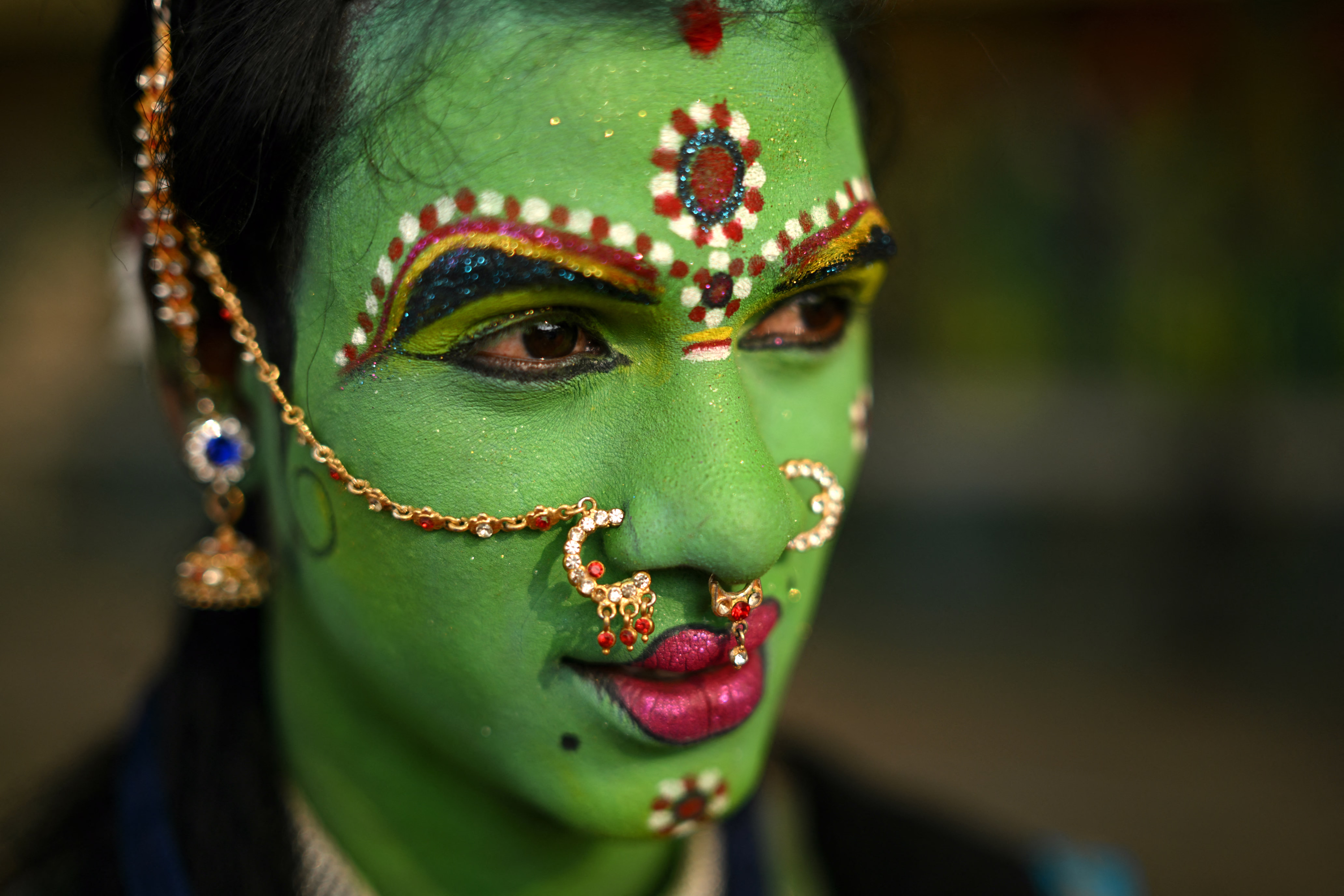 A person poses while wearing ornately decorated green make up on their face.