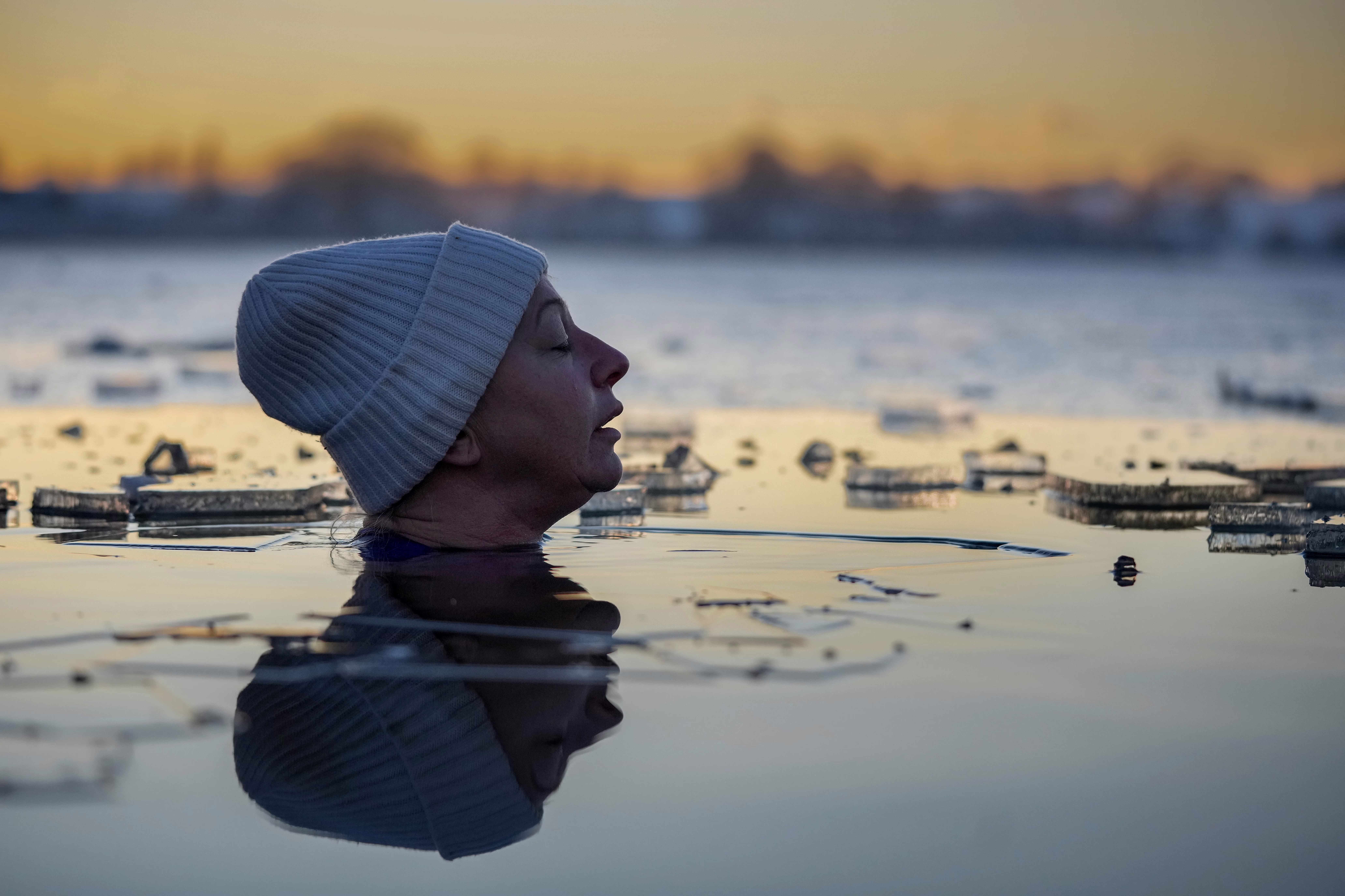 A close view of the head of a swimmer fully immersed in a lake, surrounded by ice
