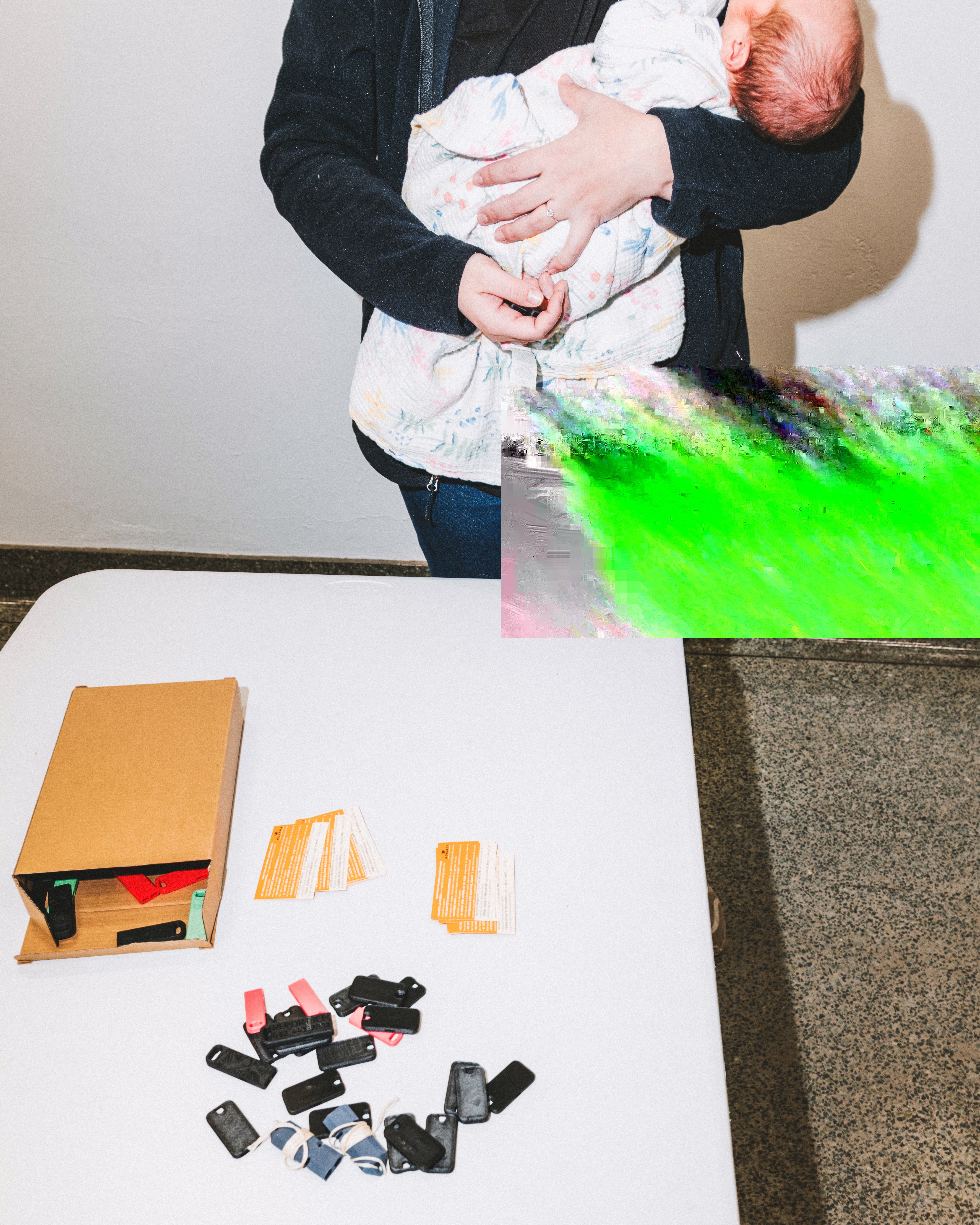 A woman holding a baby stands in front of a table with ICE whistles on it