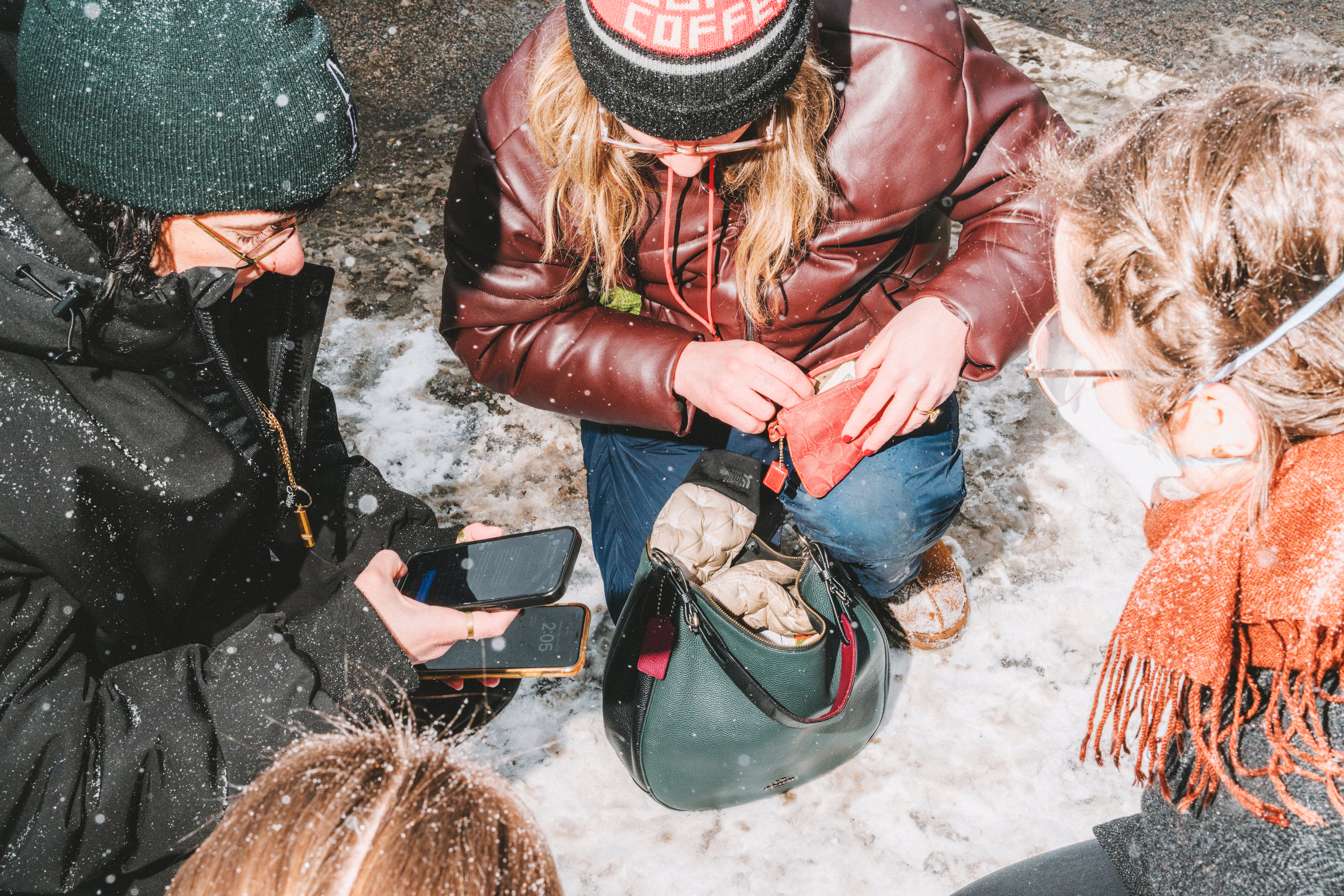 Three women crouch on the ground with their phones during a protest