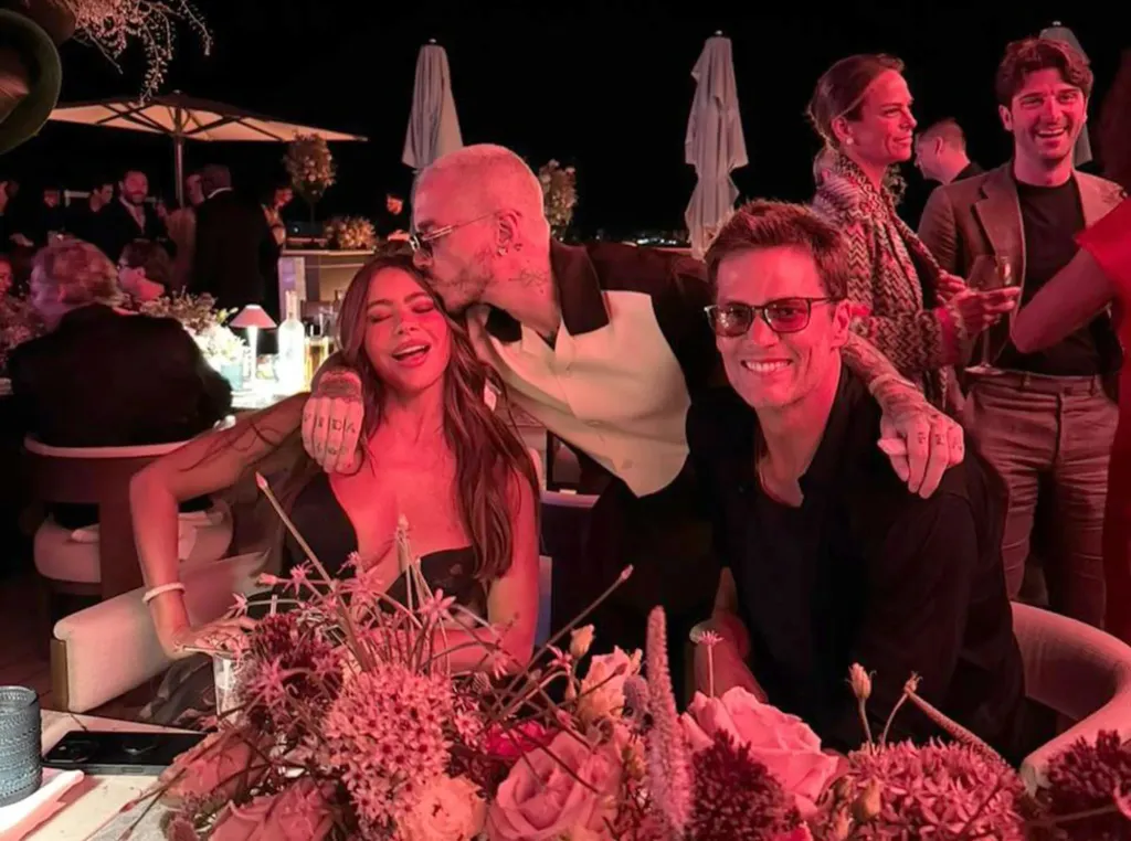 Sofia Vergara, a man kissing her head, and Tom Brady smiling at a table with flowers.