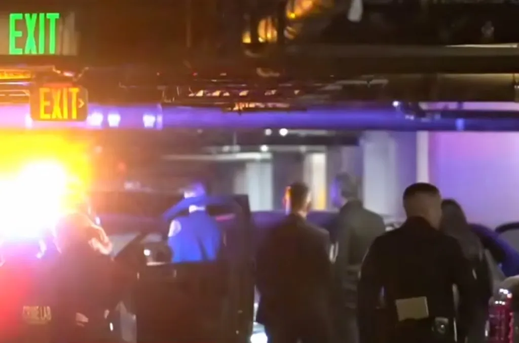 Police officers and emergency lights at a crime scene in a parking garage.