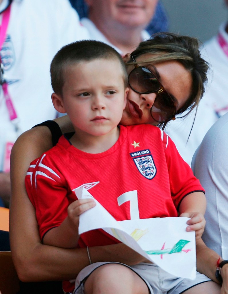 Victoria Beckham , in sunglasses, with her young son Brooklyn, in a red England jersey, at a soccer match.