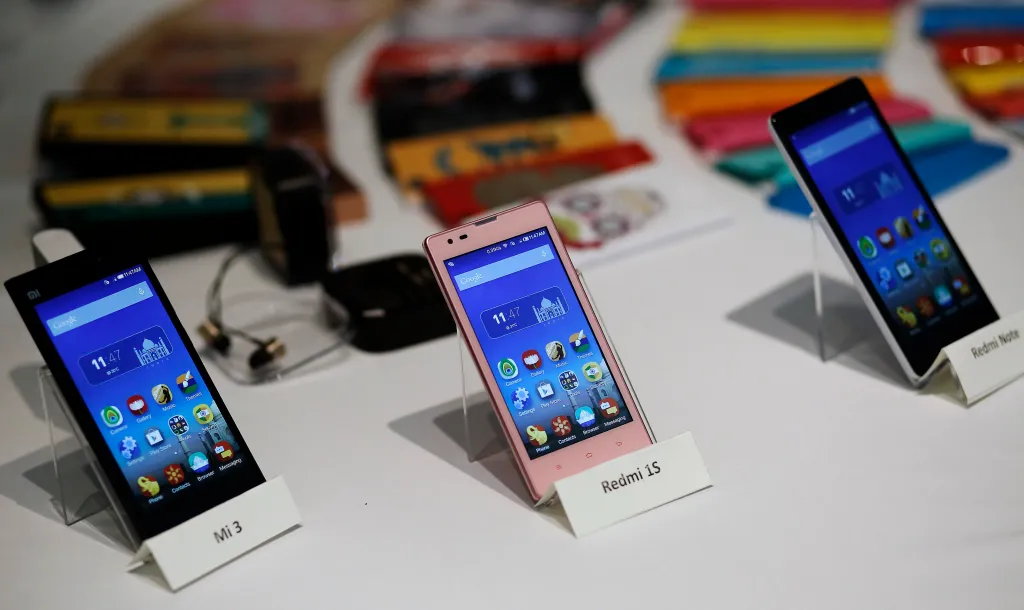 Three Xiaomi Mi phone models (Mi 3, Redmi 1S, and Redmi Note) displayed on white stands at their launch.