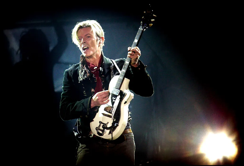 David Bowie performing on stage with an electric guitar.