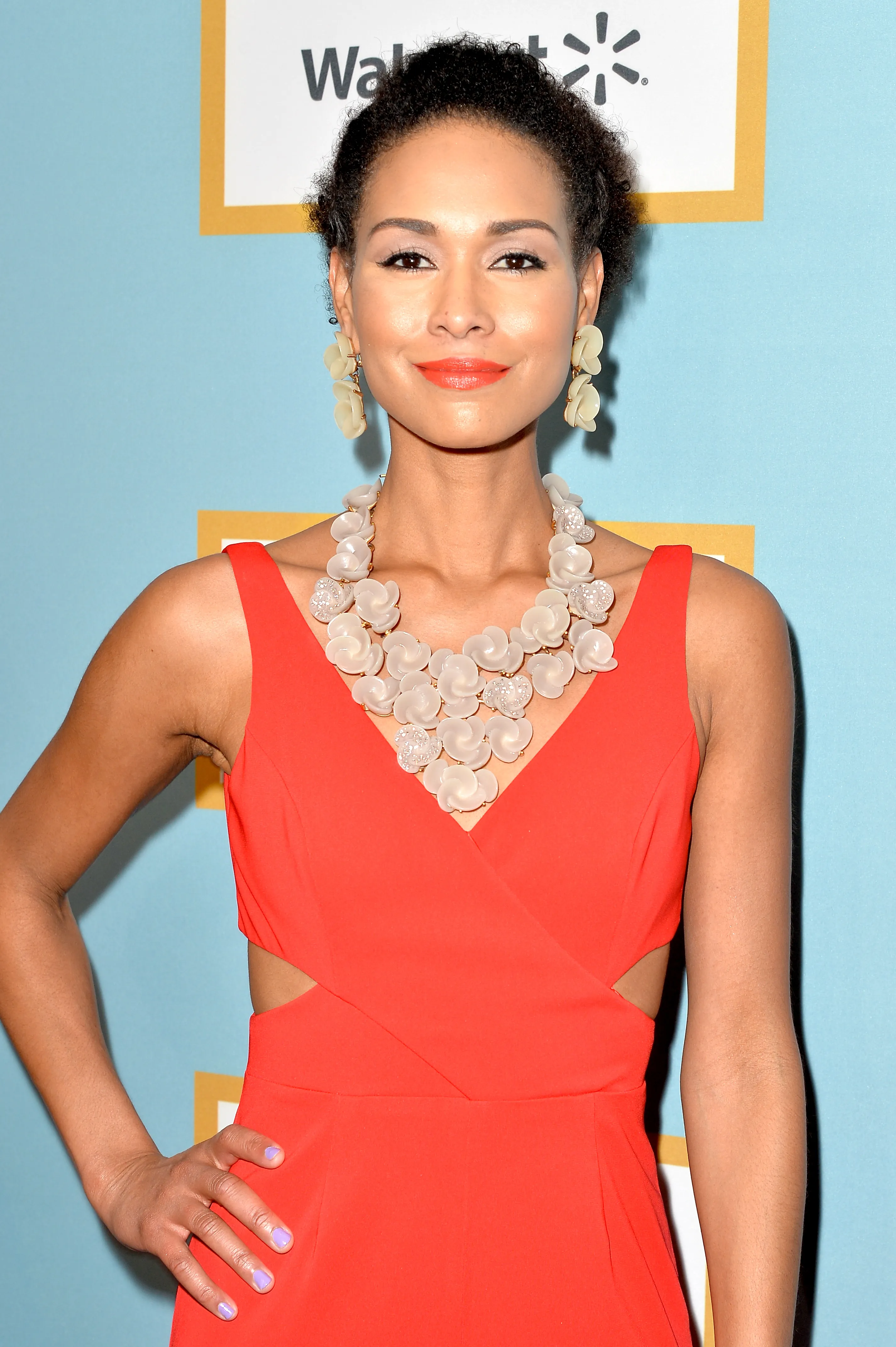 Katie Rost wearing an orange dress with a white floral necklace and earrings.