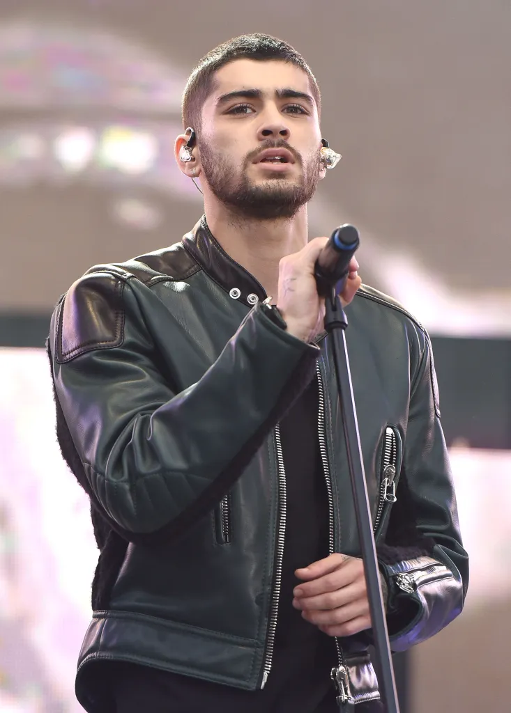 Zayn Malik performing on stage, wearing a black leather jacket and holding a microphone.