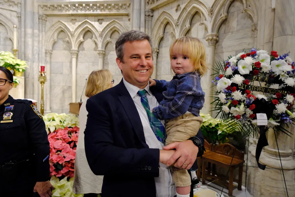 NYPD Captain Conor McDonald, the son of late Detective Steven McDonald, holds a child during a memorial service honoring his father.