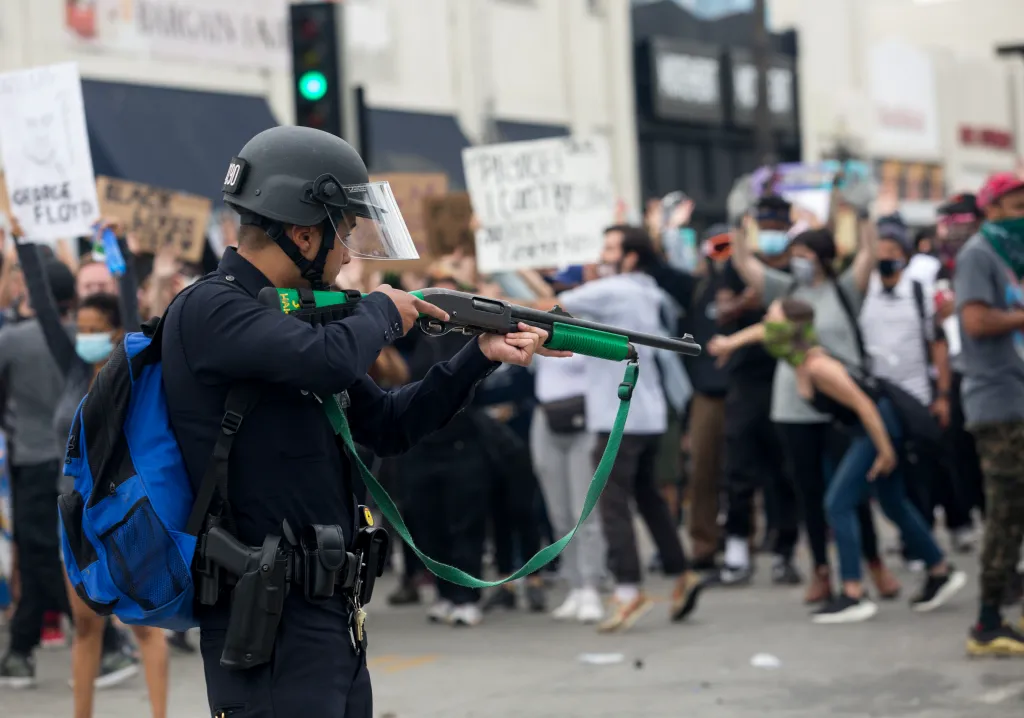 A police officer aiming a riot control gun at protestors.