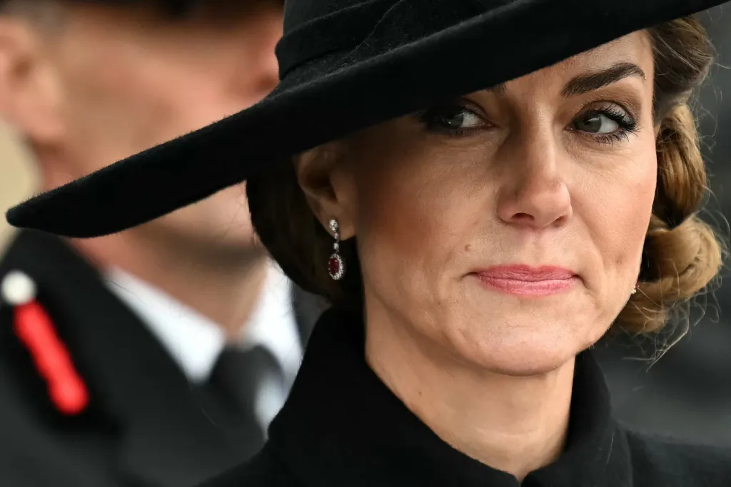 Catherine, Princess of Wales, wearing a black hat and coat, and diamond and ruby earrings at an Armistice Day service.