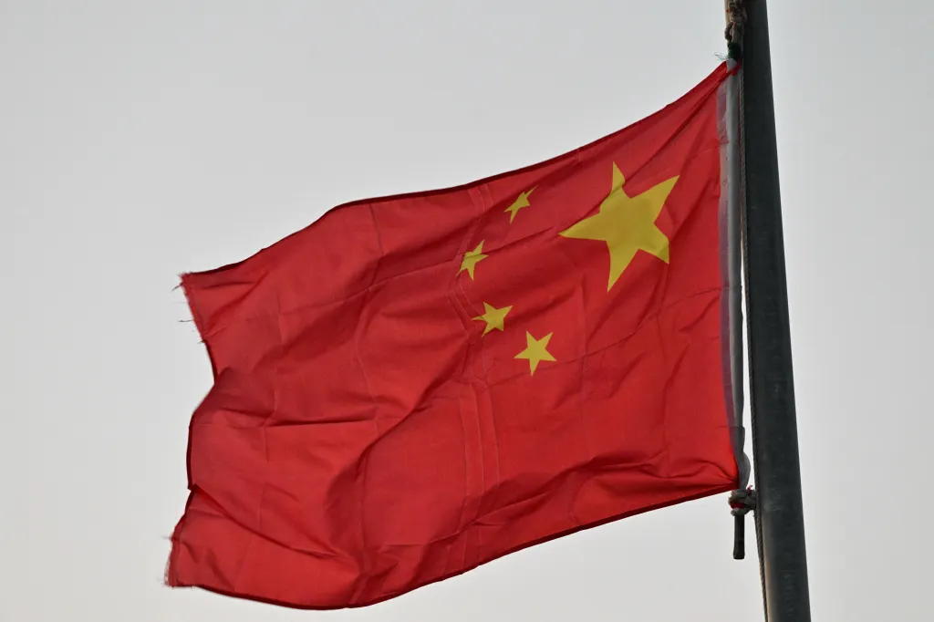 The red flag of China, with five yellow stars, waving against a light sky.