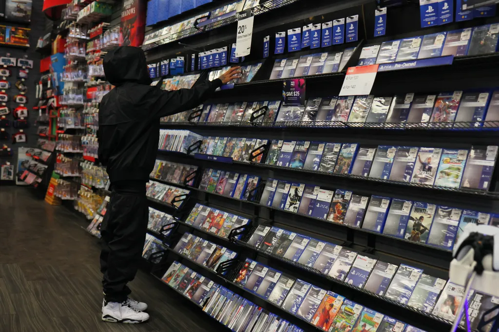 A person in a black hoodie and white sneakers shops for PlayStation games at a GameStop store.