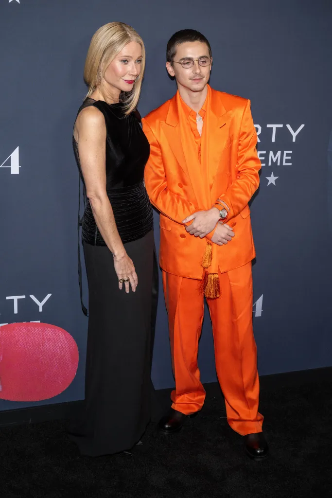 Gwyneth Paltrow in a black gown and Timothee Chalamet in an orange suit pose at the 
