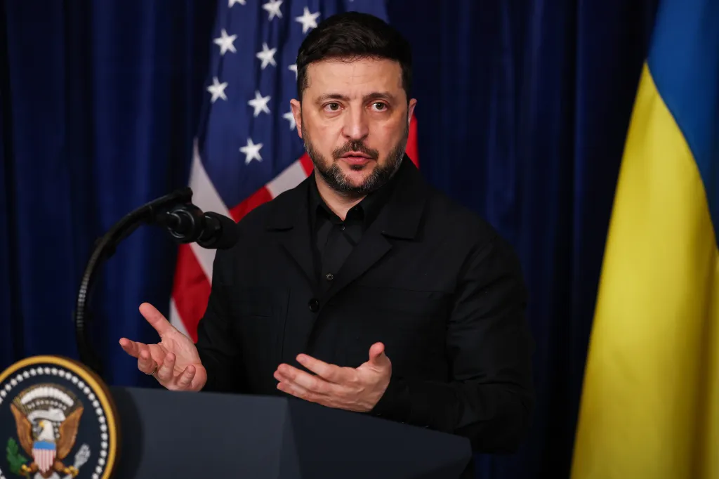 Ukrainian President Volodymyr Zelensky speaking at a podium with US and Ukrainian flags behind him.
